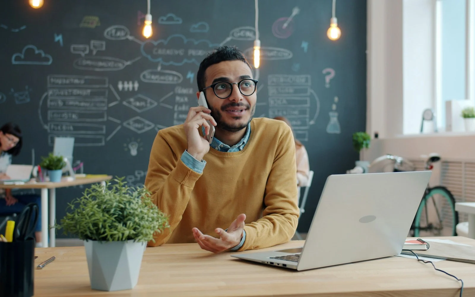 Homem sorrindo ao telefone em frente ao notebook em um escritório