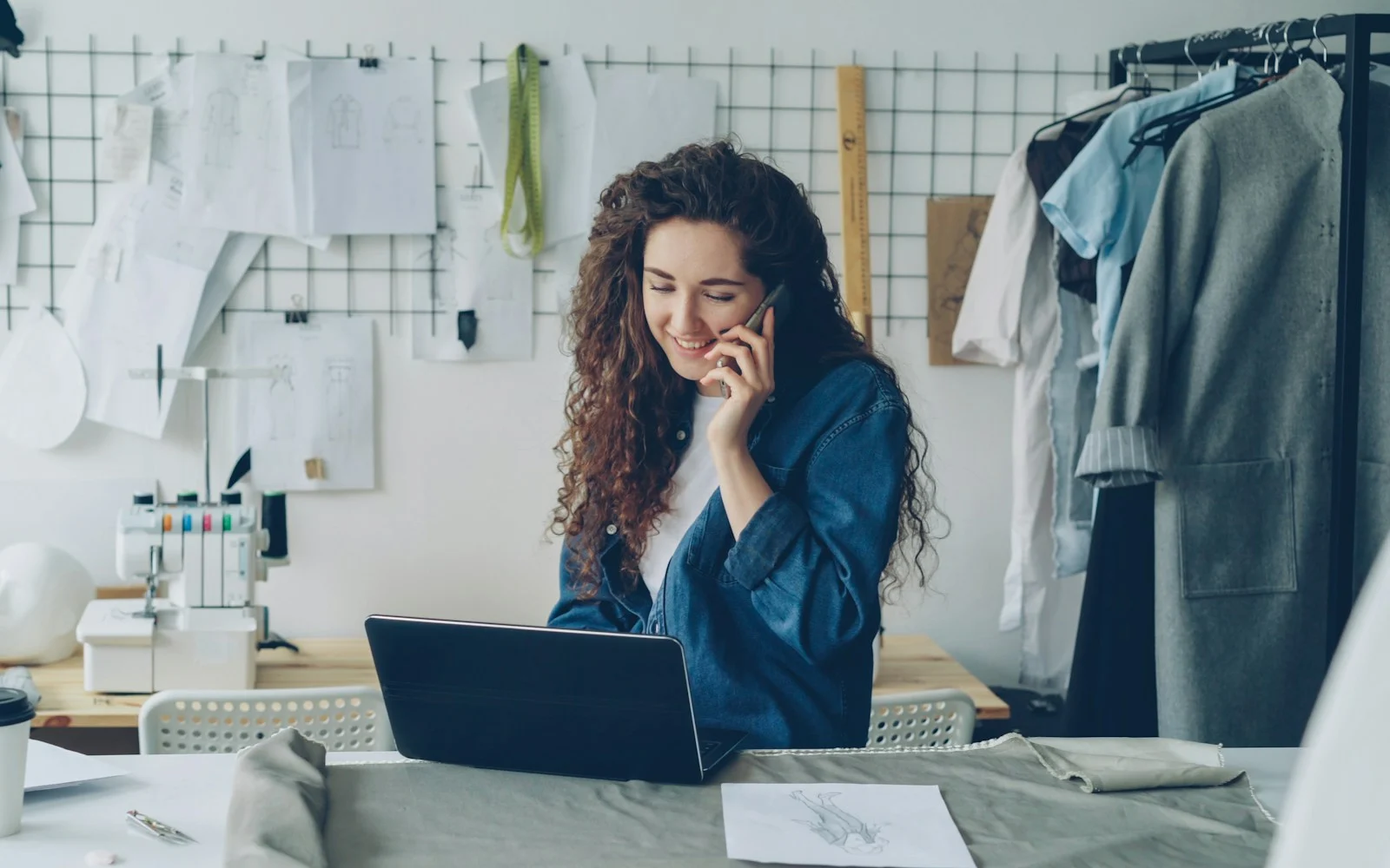 Empreendedora ao telefone trabalhando no notebook em seu ateliê